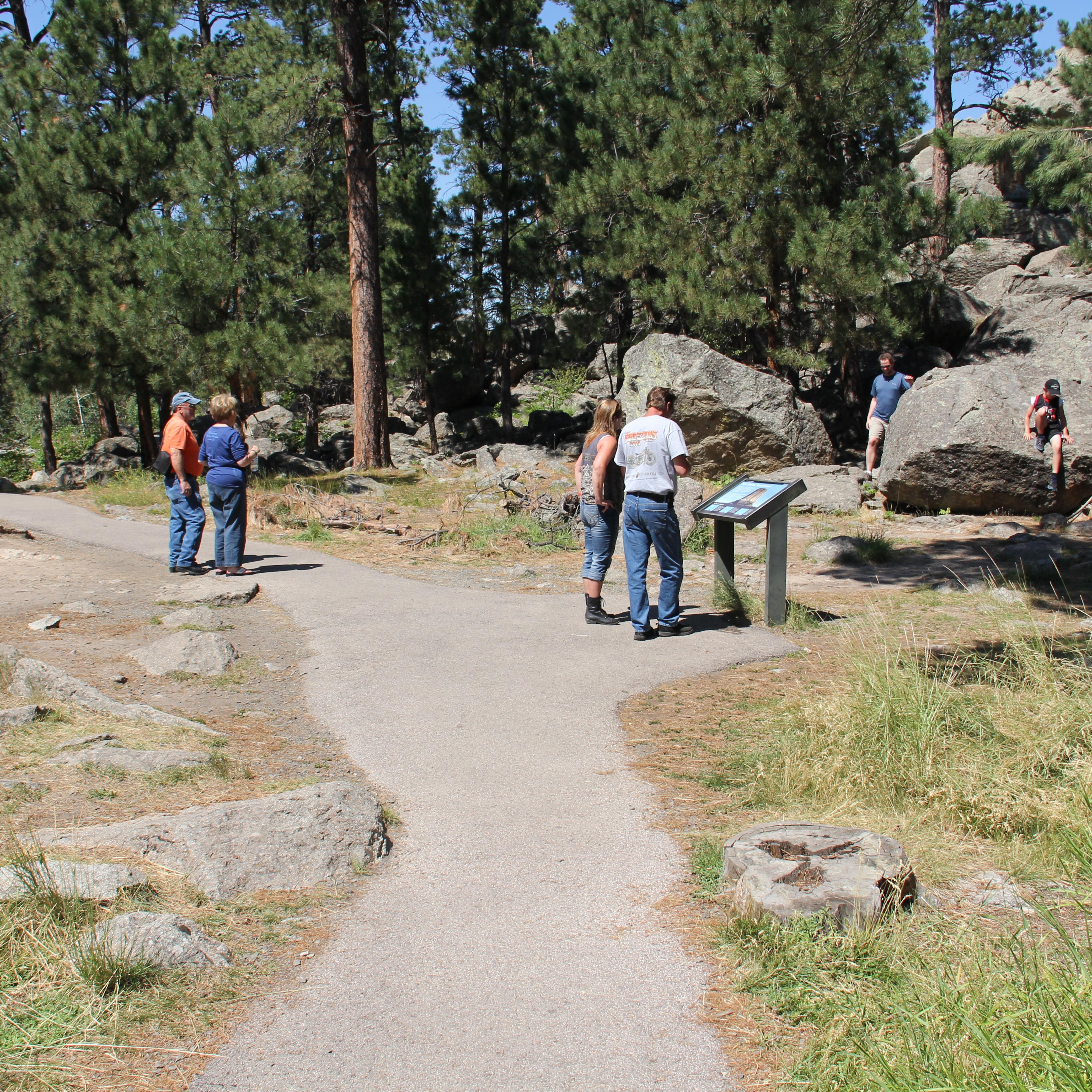 several visitors on paved path looking at wayside exhibit and surrounding scenery