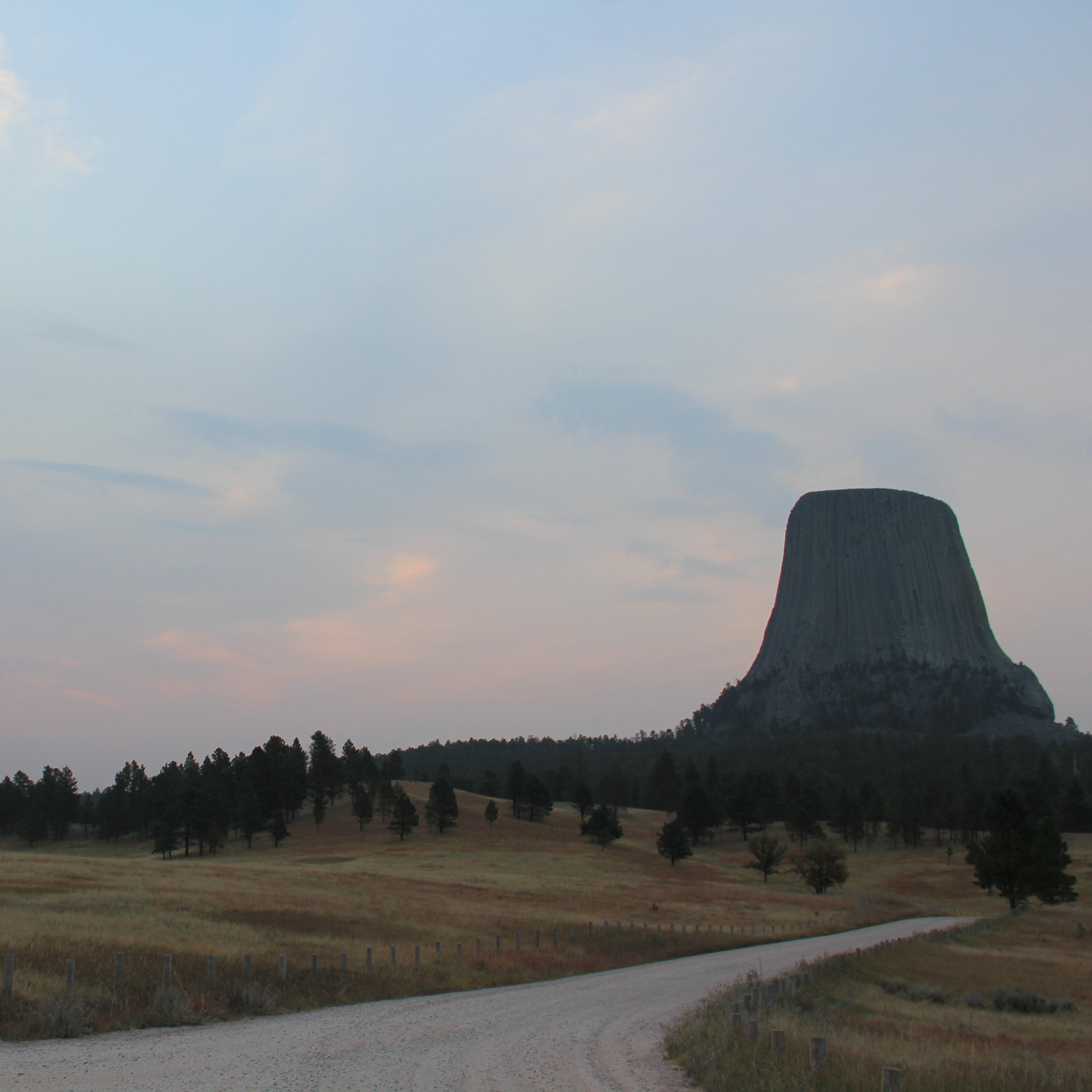 a pink sun rises into a cloudy morning sky with Devils Tower
