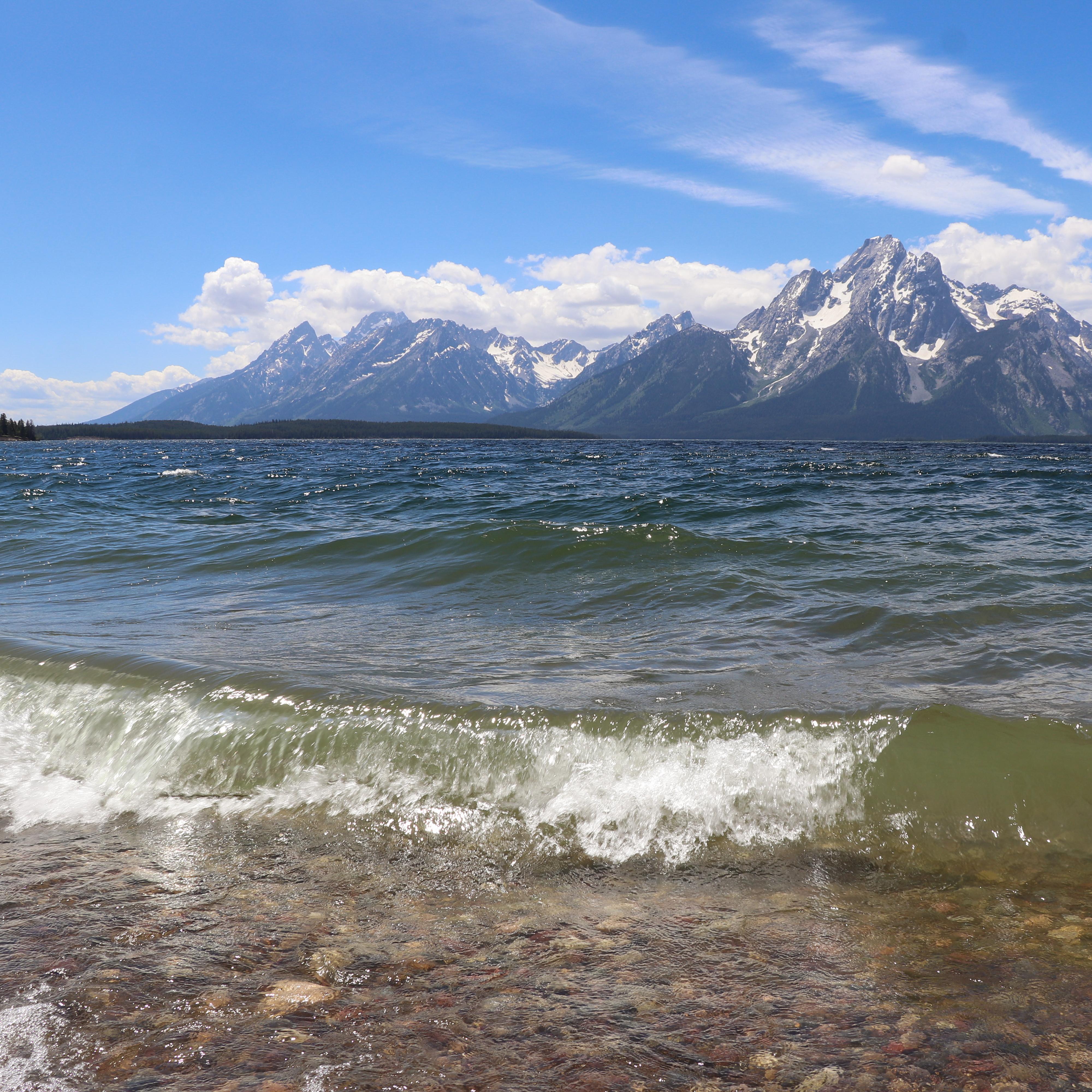 Waves crash on the shore of a lake at the base of a mountain range.