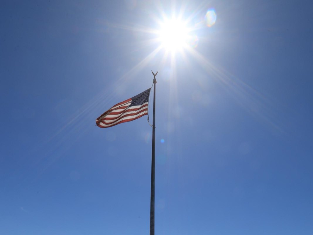 American flag backlit by the sun in front of a blue sky.