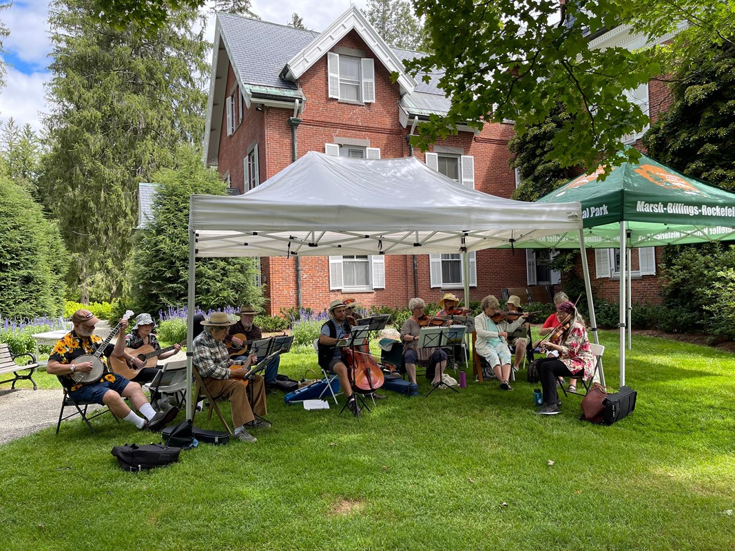 Orchestra performs outdoors under tents in front of mansion