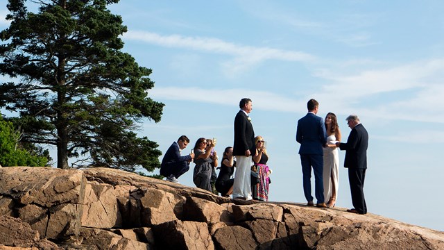 A bride and groom stand on a cliff with a small group of people