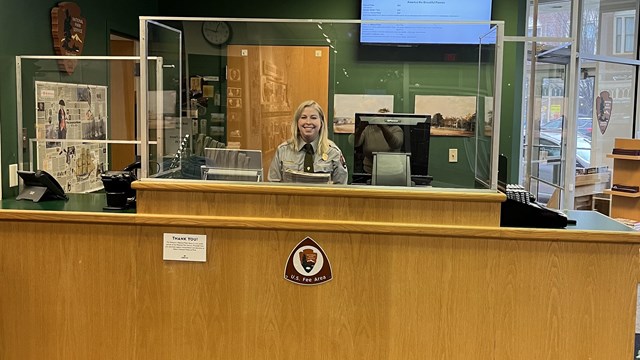 Image of the interior of the Visitor Center with a smiling ranger behind the desk 