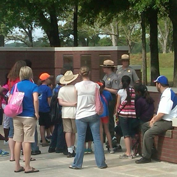 A ranger in green and gray uniform leading students on a tour in the courtyard.