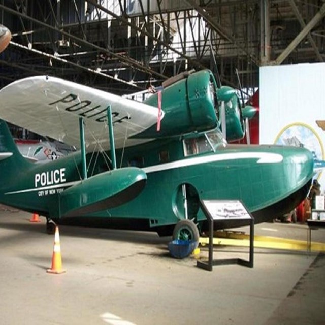 Small green police plane in a hangar with museum signage in front of it
