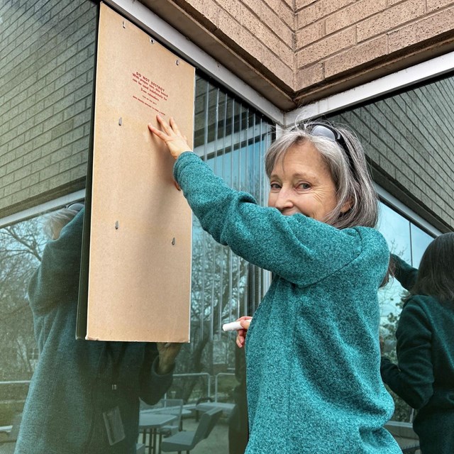 a woman uses a straight edge to make markings on a window