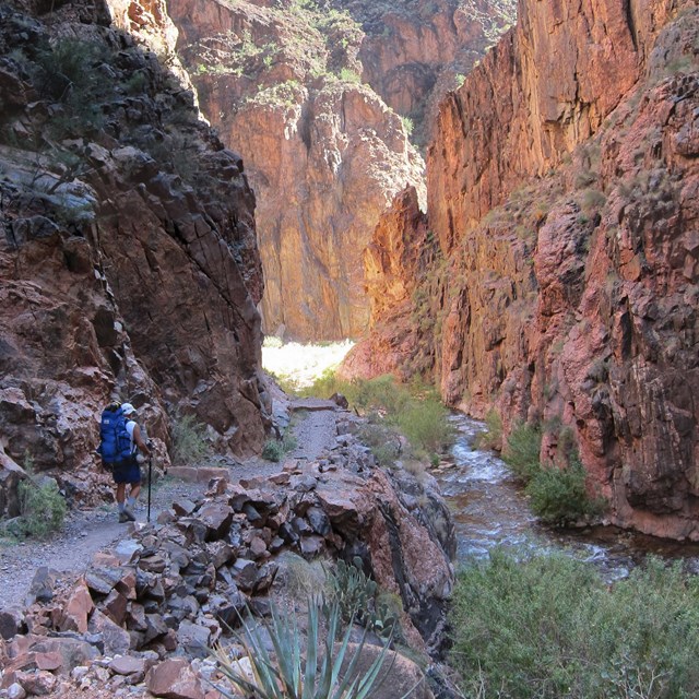 Photo of a hiker walking down a trail in a steep sided canyon.
