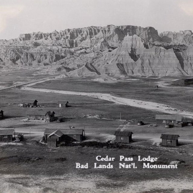 a historic black and white photo of a lodge and cabins in front of badlands buttes.