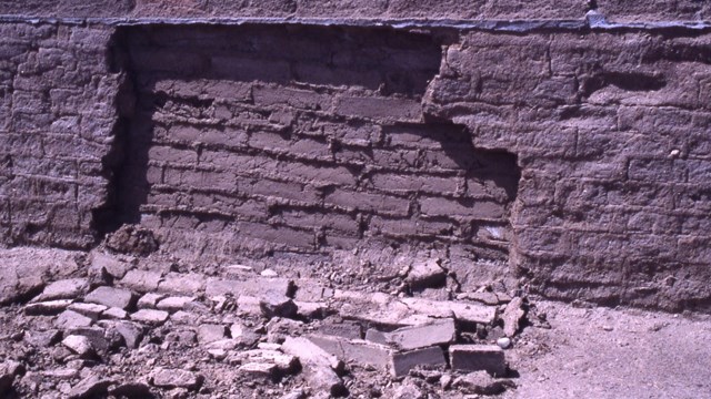 A section of an adobe brick wall has collapsed forward, exposing an inner wall. 