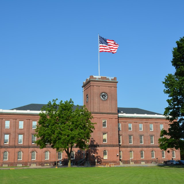 A three-story brick building with a tower built in the center of the facade. The tower has a clock.