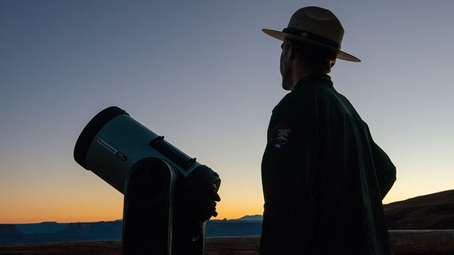 Silhouette of a ranger using a telescope to look up at the night sky.