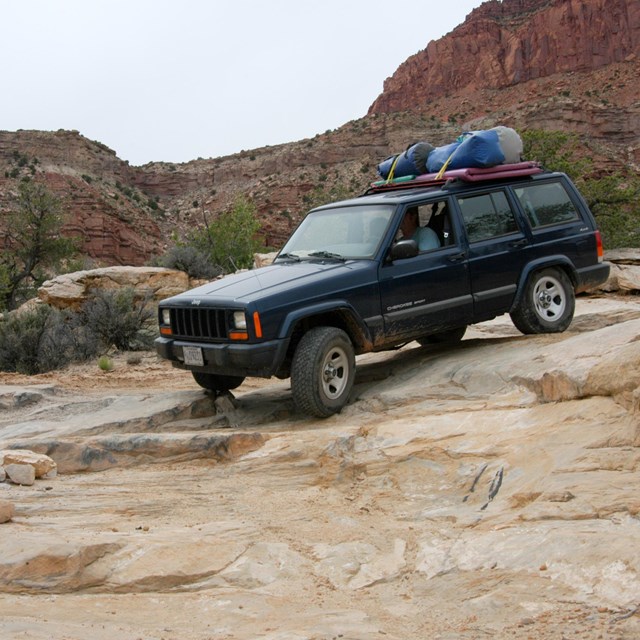 a blue Jeep drives over slickrock