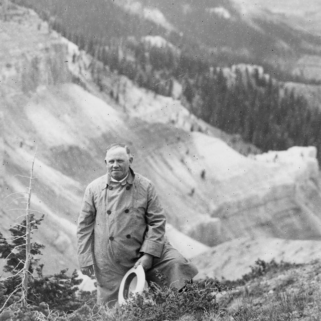 Black and white photo of man posing before a landscape. 