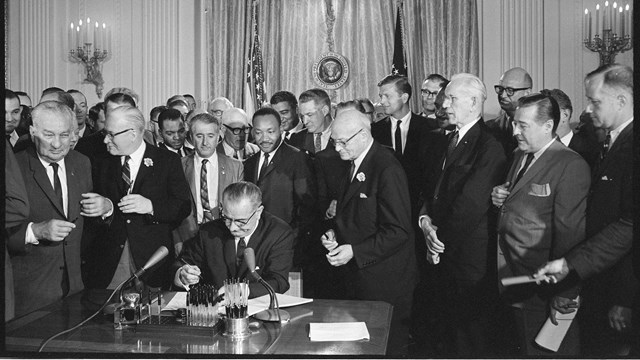 President Lyndon Johnson signing a bill with a large crowd standing behind his desk