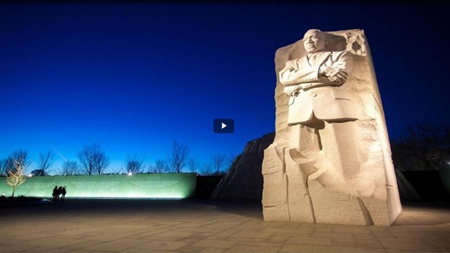Video screen capture of a tall statue of Dr. Martin Luther King, Jr. at night