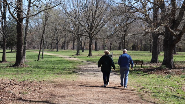 Two visitors walk on dirt road in spring.  
