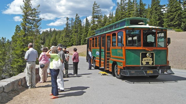 At an overlook, visitors stand along a 2 foot native stone wall next to a trolley near trees