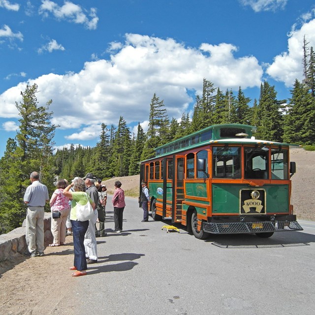 At an overlook, visitors stand along a 2 foot native stone wall next to a trolley near trees