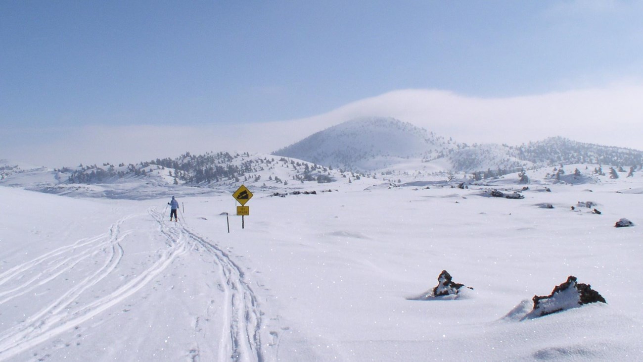 A skier traverses a snowy road surrounded by snow covered lava features. 