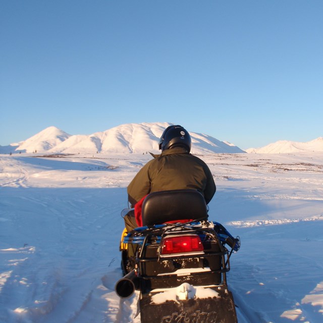 a person riding a snowmobile in a snowy, mountainous landscape