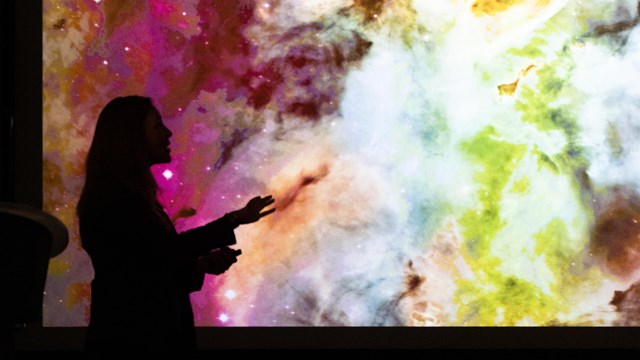 The black side profile silhouette of a woman in front of a screen with a colorful image of a galaxy 