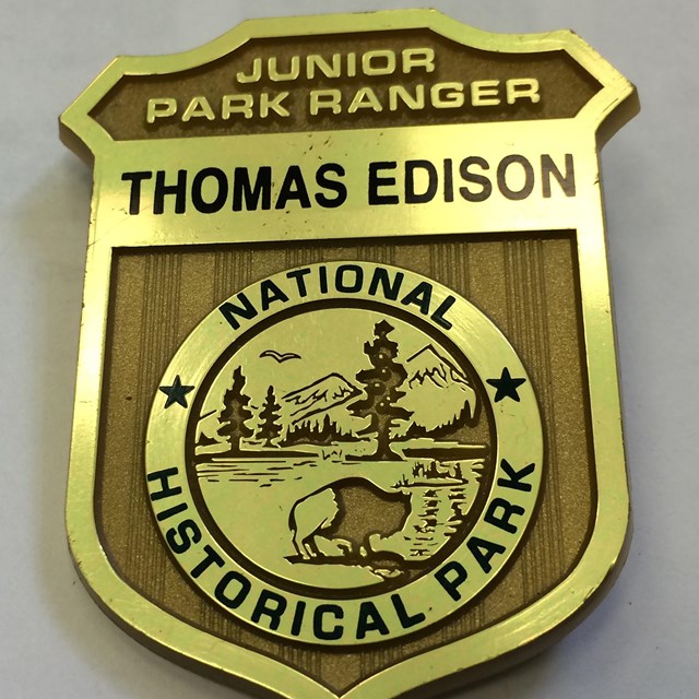 Plastic gold badge that has inscribed Junior Park Ranger - Thomas Edison National Historical Park.