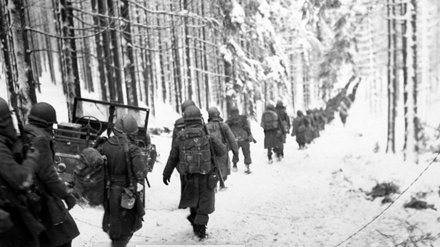 A black and white image of soldiers marching through snow covered woods