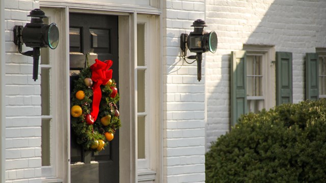 A color image showing a wreath on a black door of a white brick house