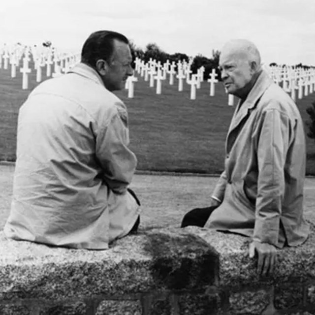 Walter Cronkite seated to the left of Dwight Eisenhower on a stone wall.
