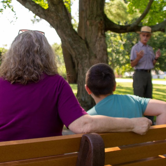 Woman and child seated on a bench facing a park ranger.