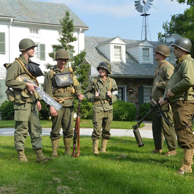 Volunteers in WWII uniforms stand in front of the Eisenhower home.