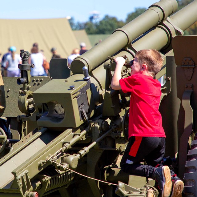 A child looking through the site on a WWII era cannon. 