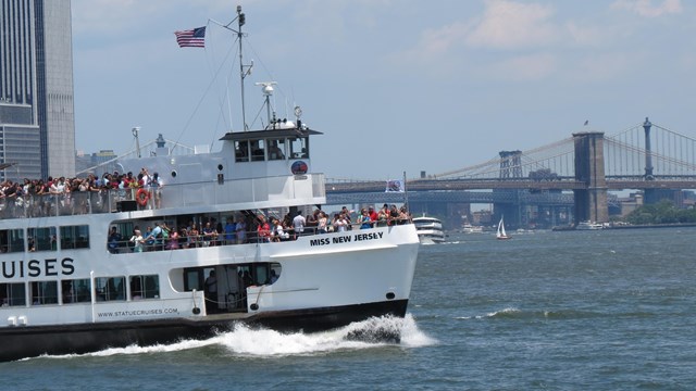 A Statue City Cruise ferry makes its way across the harbor, the Brooklyn Bridge is in the backround