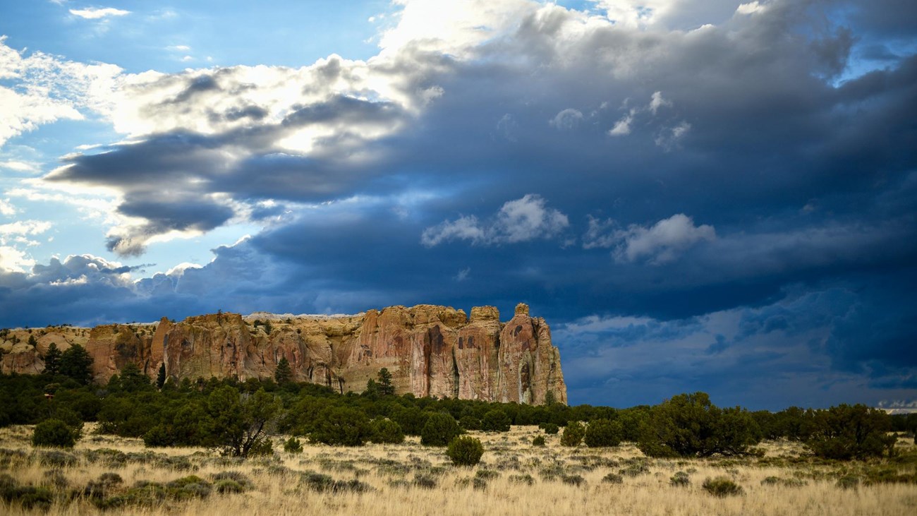 A sandstone bluff with dark storm clouds behind it.