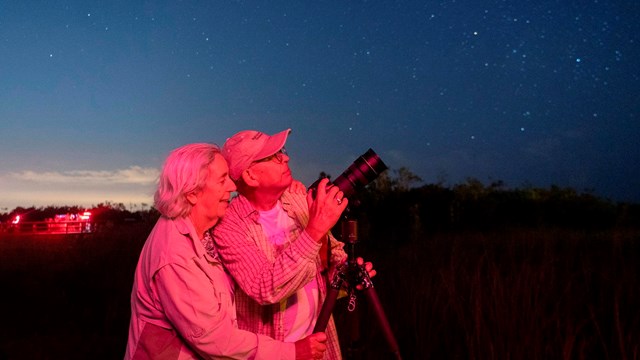 Two people stand by a camera pointed up at a dark night sky.