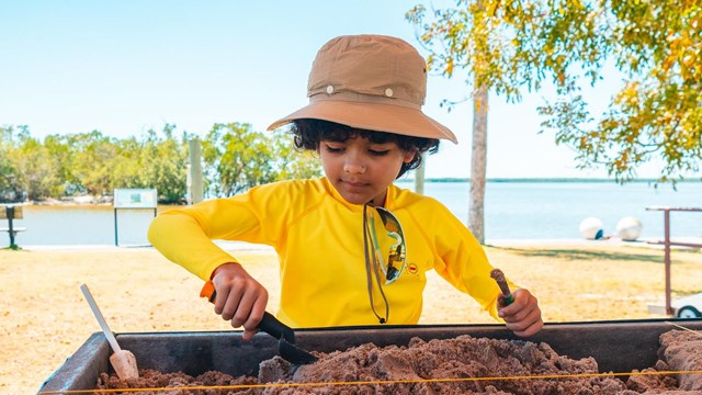 A young child uses tools to move sand in an archaeological activity hosted by the Park. 