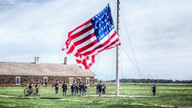 Volunteers in period uniforms lower a large U.S. flag.