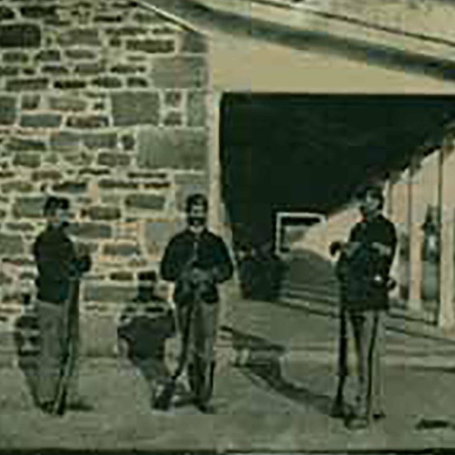 Historic image of 3 soldiers standing at the end of a sandstone building.