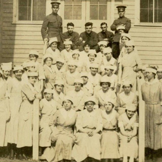 A black and white photograph of nurses and doctors on the steps of a building.