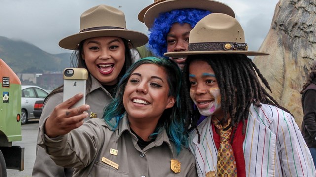 Two new Junior Rangers in clown makeup and wigs pose with rangers for a selfie.