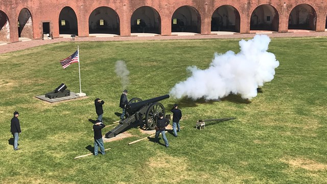 Several men in Civil War era uniforms firing a cannon inside a fort. 