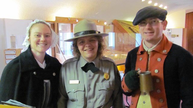 A park ranger stands with a continental soldier and a modern woman, smiling at the camera.