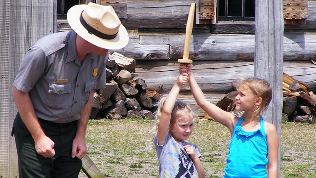 Two little girls hold up a wooden sword together.