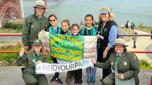 Girl scouts posing with park rangers and a sign reading "Find Your Park"