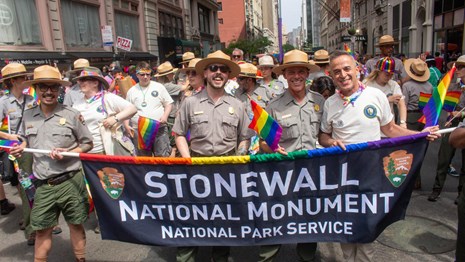Park rangers and volunteers holding a banner in a pride parade 