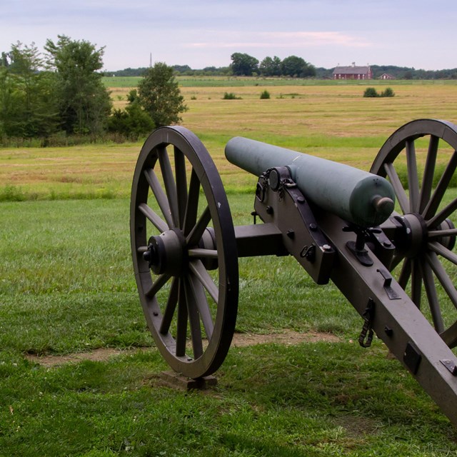 A cannon pointed into a farm field with a low ridge in the far distance.