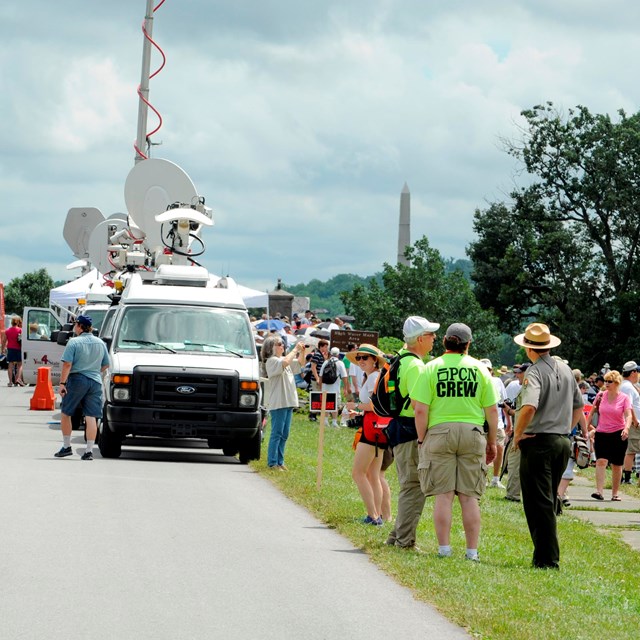 A park ranger talks to a TV crew alongside of a park roads. Press trucks line the road behind them.
