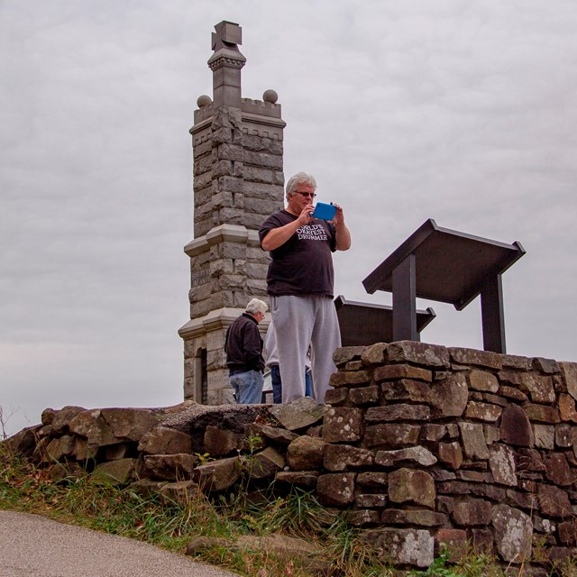 A photo of a tall granite monument behind a small group of visitors as they read a sign.