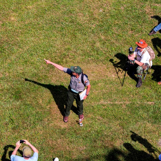 As seen from above, a park ranger points as a group of visitors watches during a ranger program. 