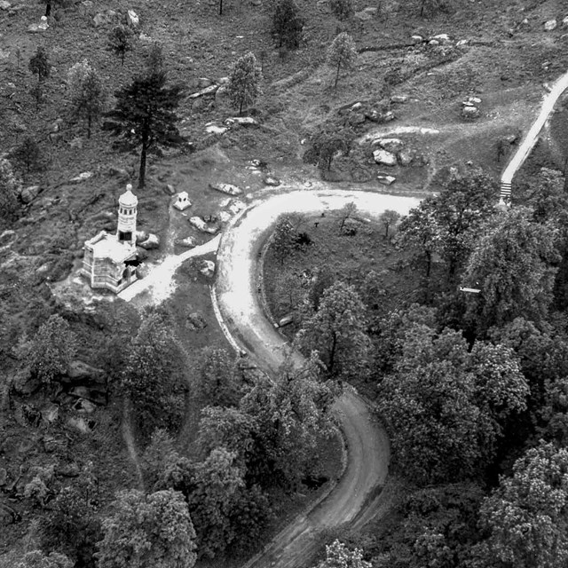 An overhead black and white photo of a large castle-like structure on top of a tree covered hill. 